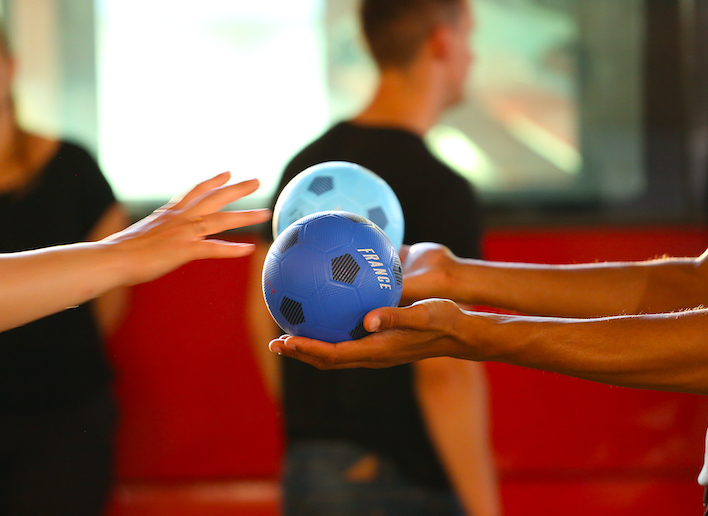 Main d'une personne qui tend un ballon bleu vers la main d'une autre personne